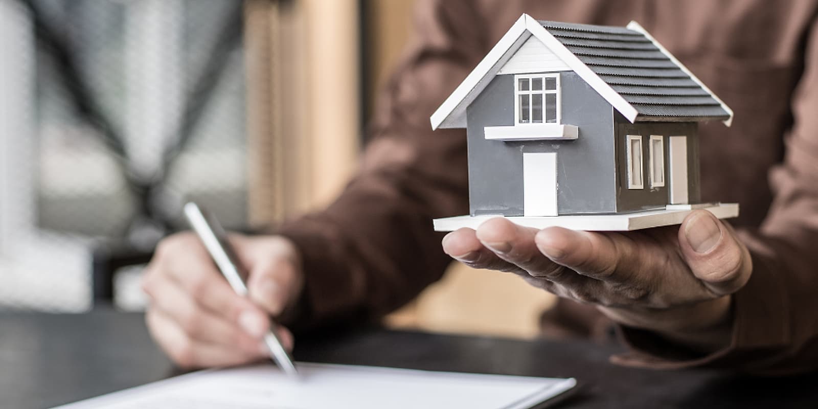 Pessoa assinando um contrato imobiliário segurando a maquete de uma casa