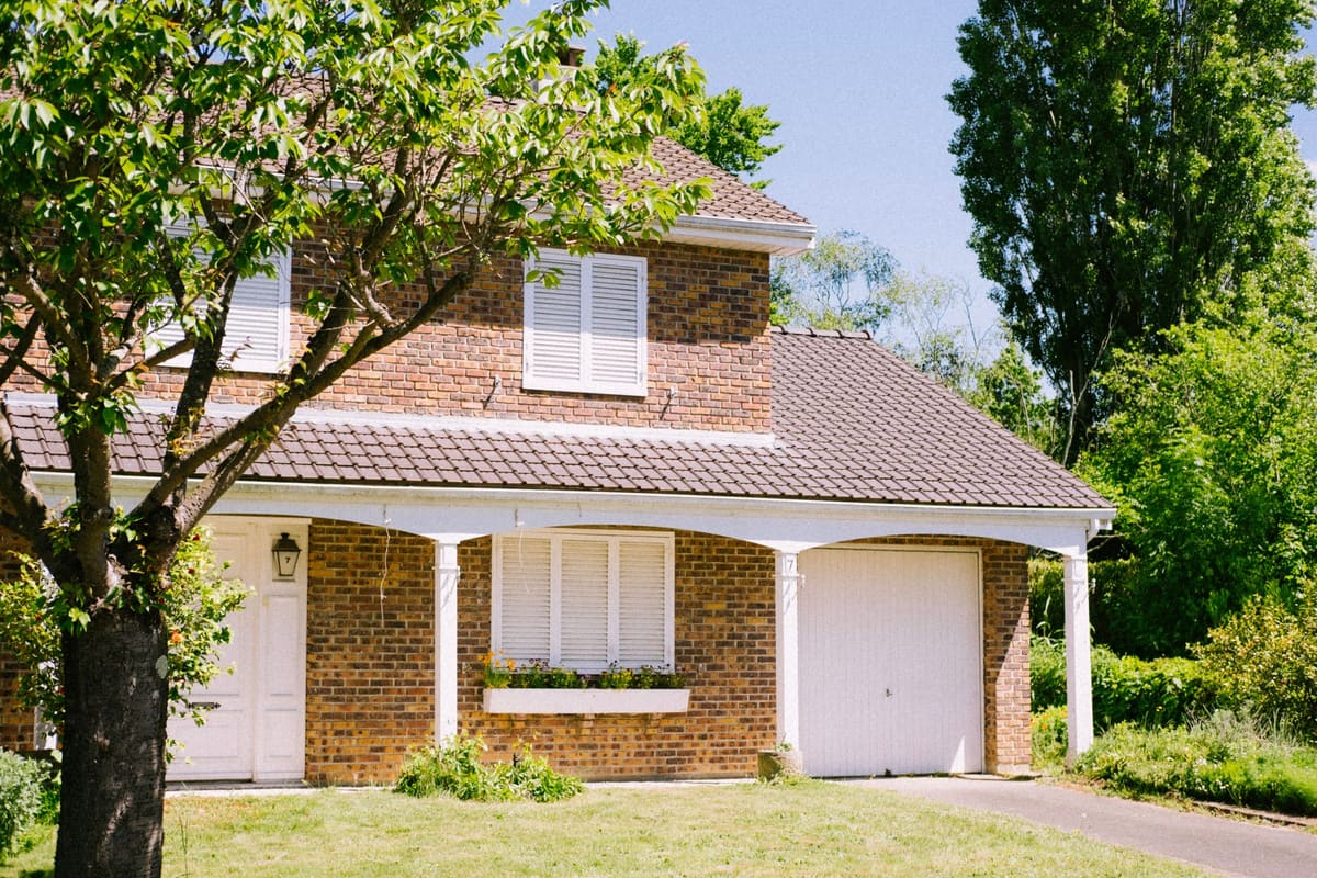 Fachada de uma casa de tijolos com garagem, jardim e uma árvore na frente