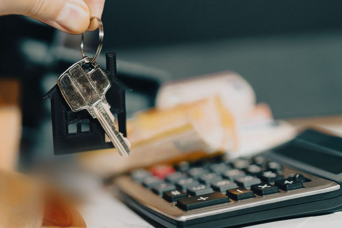 Chave de um imóvel com chaveiro de casinha ao lado de uma calculadora